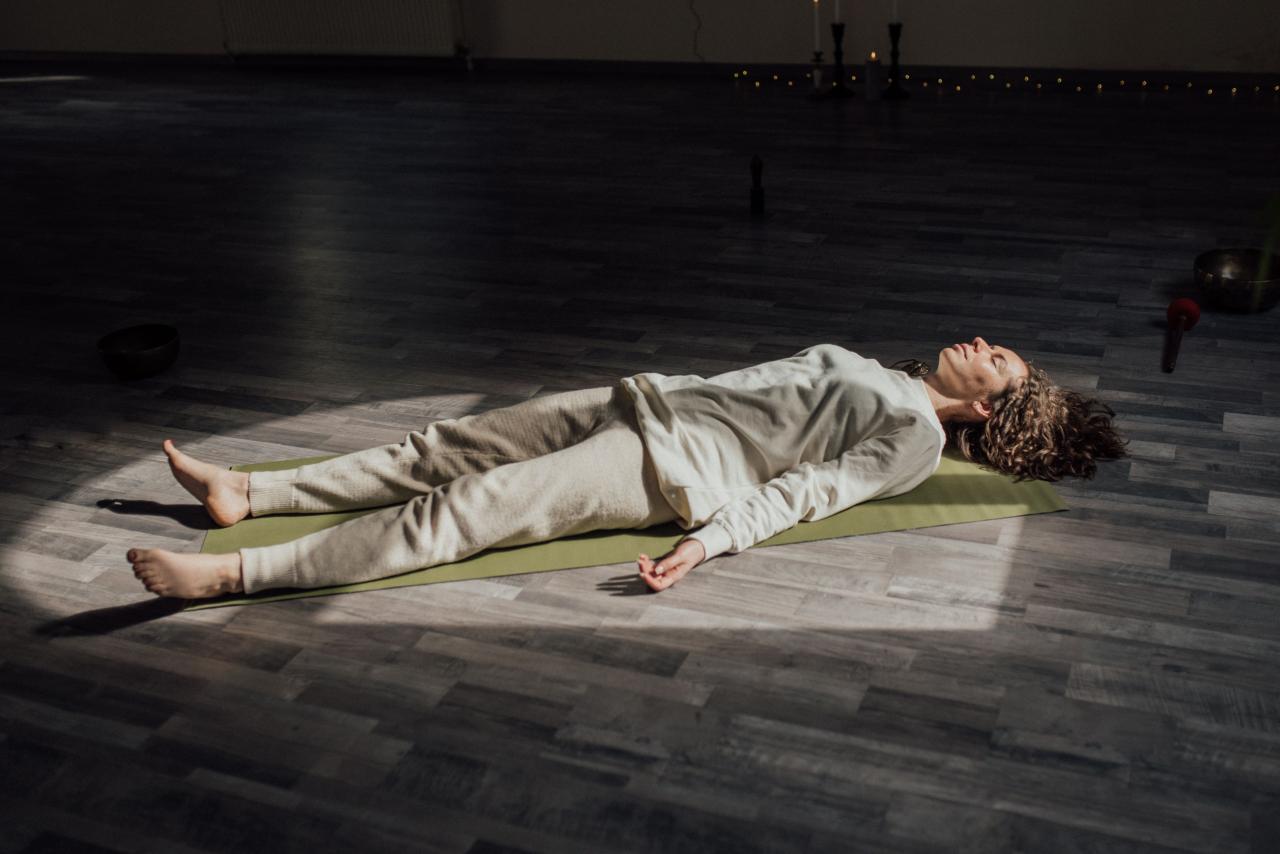 Perempuan berbaring telentang di atas matras yoga sambil melakukan latihan pernapasan dalam.